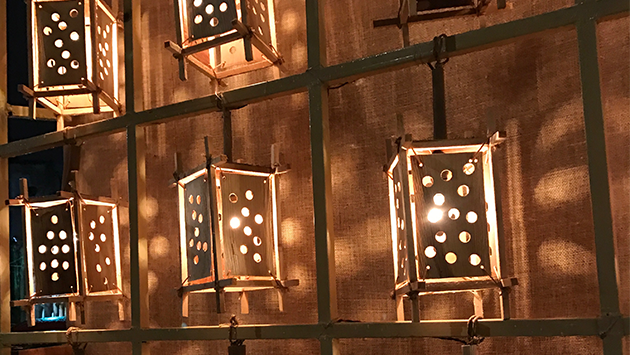 A low-light photograph of a grid of wooden lanterns with circles on each side letting out light.